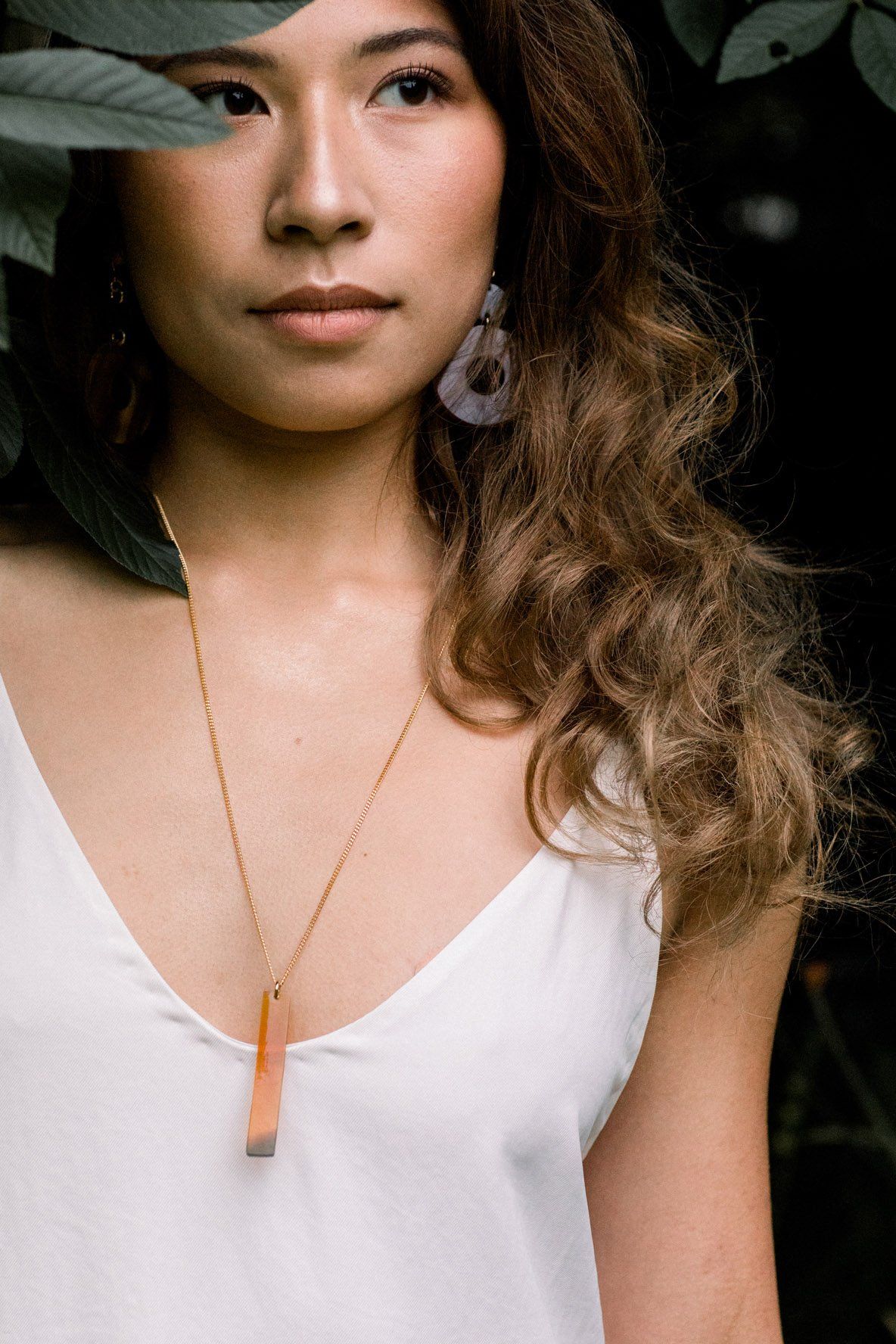 Model wearing a 16K Gold-Plated Buffalo Horn Pendant Necklace amidst greenery.