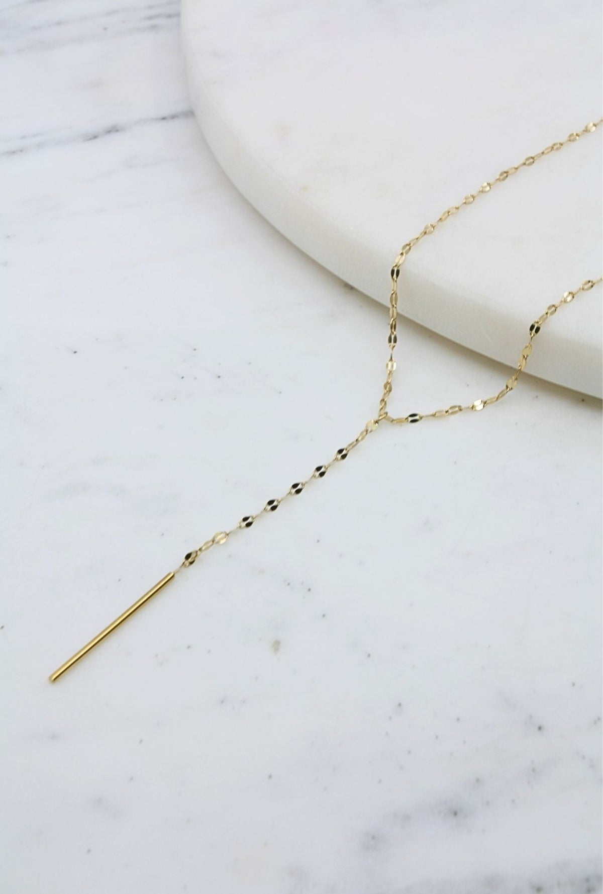 Chain Tassel Drop Necklace featuring a delicate gold chain with a minimalist drop design on a marble surface.