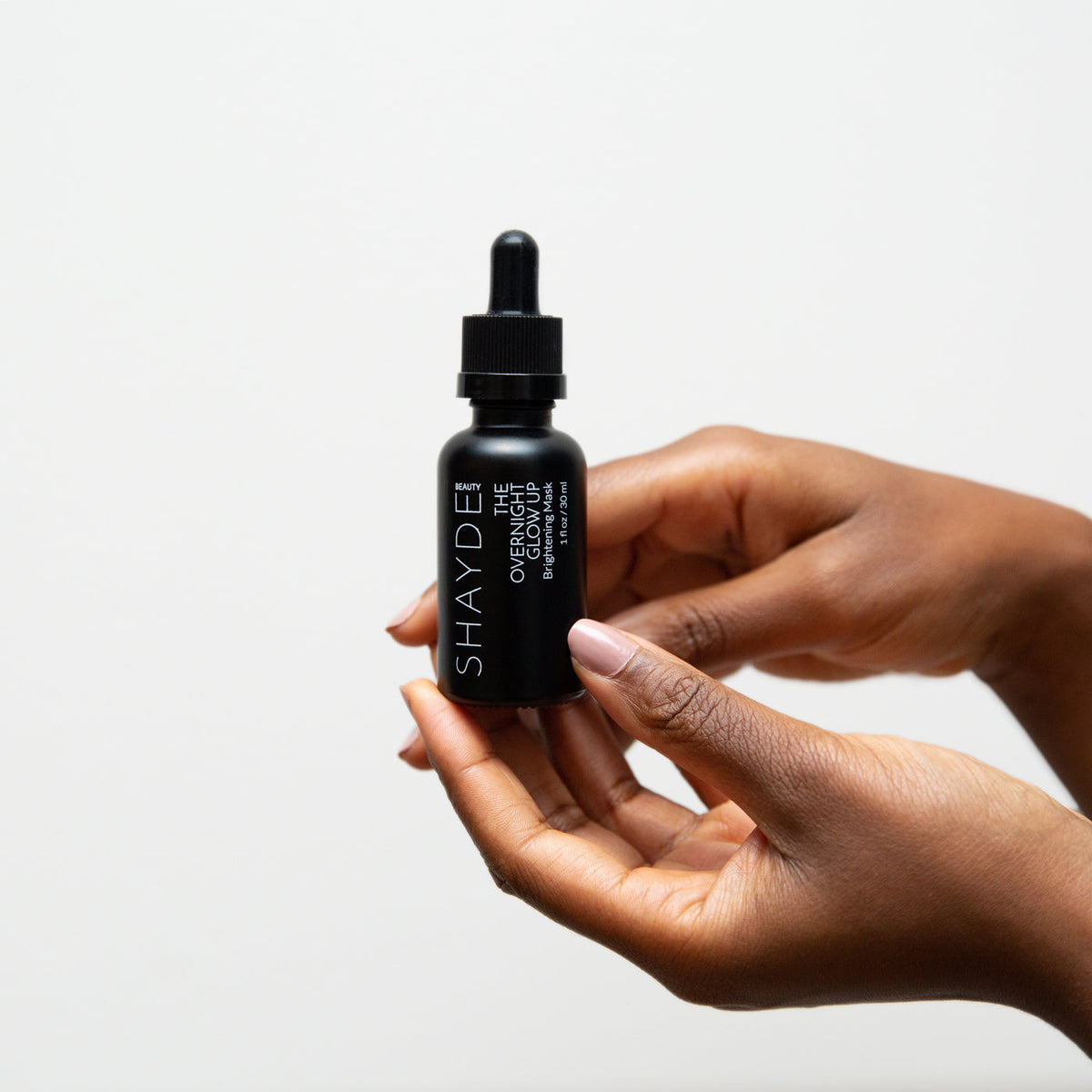 An individual holding the SHAYDE Overnight Glow Up liquid mask in a dropper bottle against a neutral background.