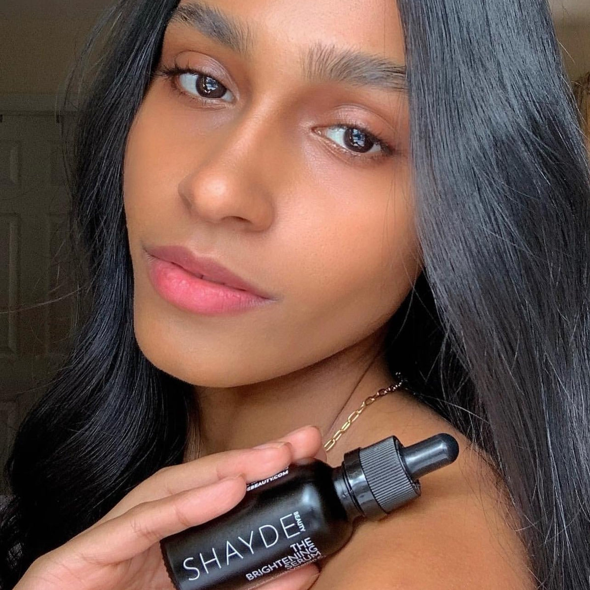 Model holding THE VITAMIN C BRIGHTENING SERUM with glowing skin, promoting radiant complexion.