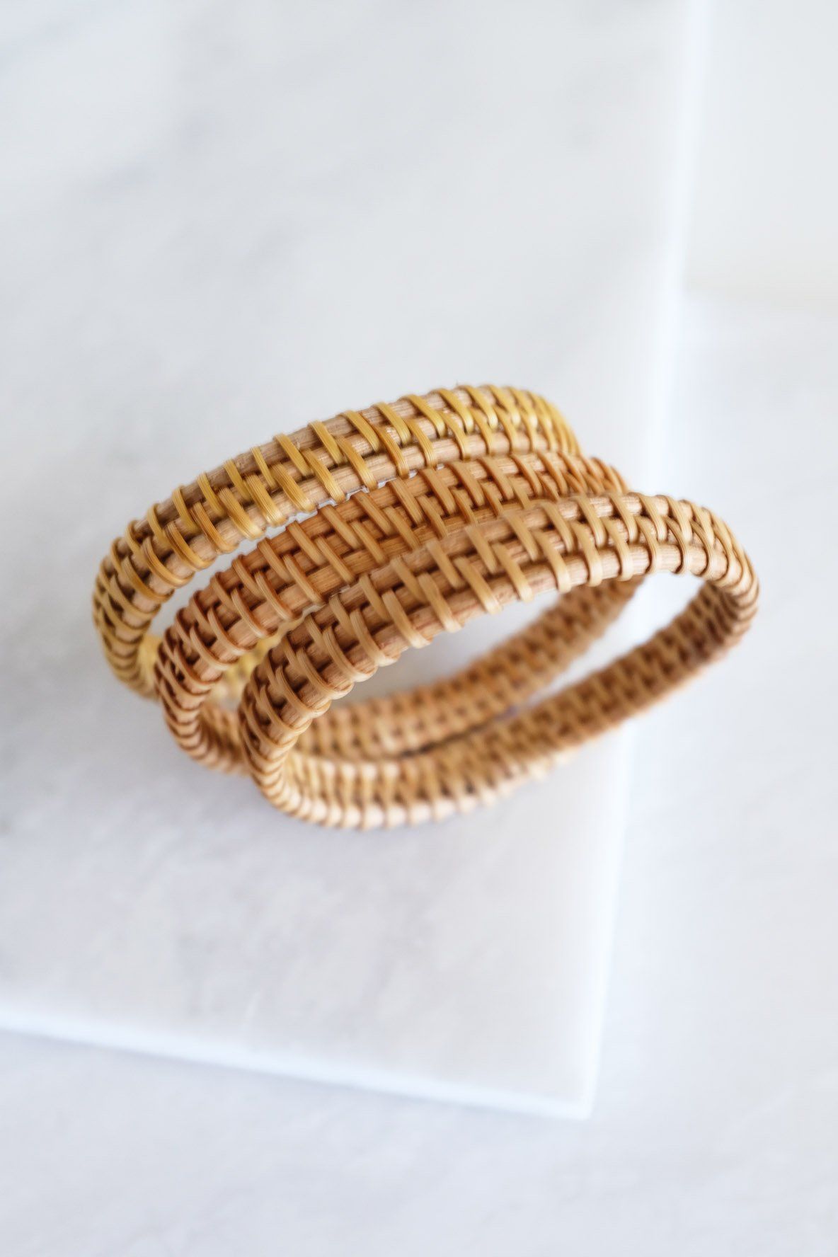 Natural Rattan Bangle Bracelets in a handwoven design, showcasing a 3-piece set on a marble surface.
