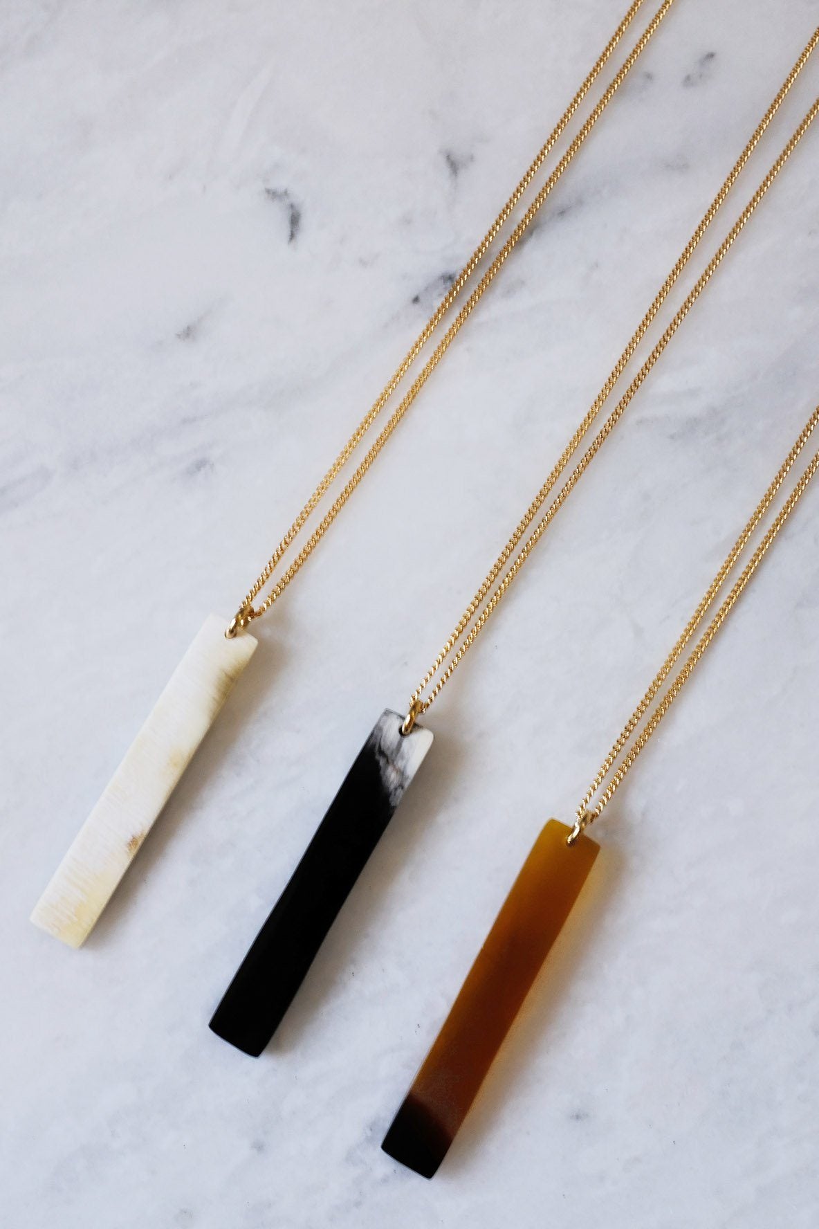 Buffalo Horn Pendant Necklace showcasing gold-plated minimalist bar necklaces on a marble surface.