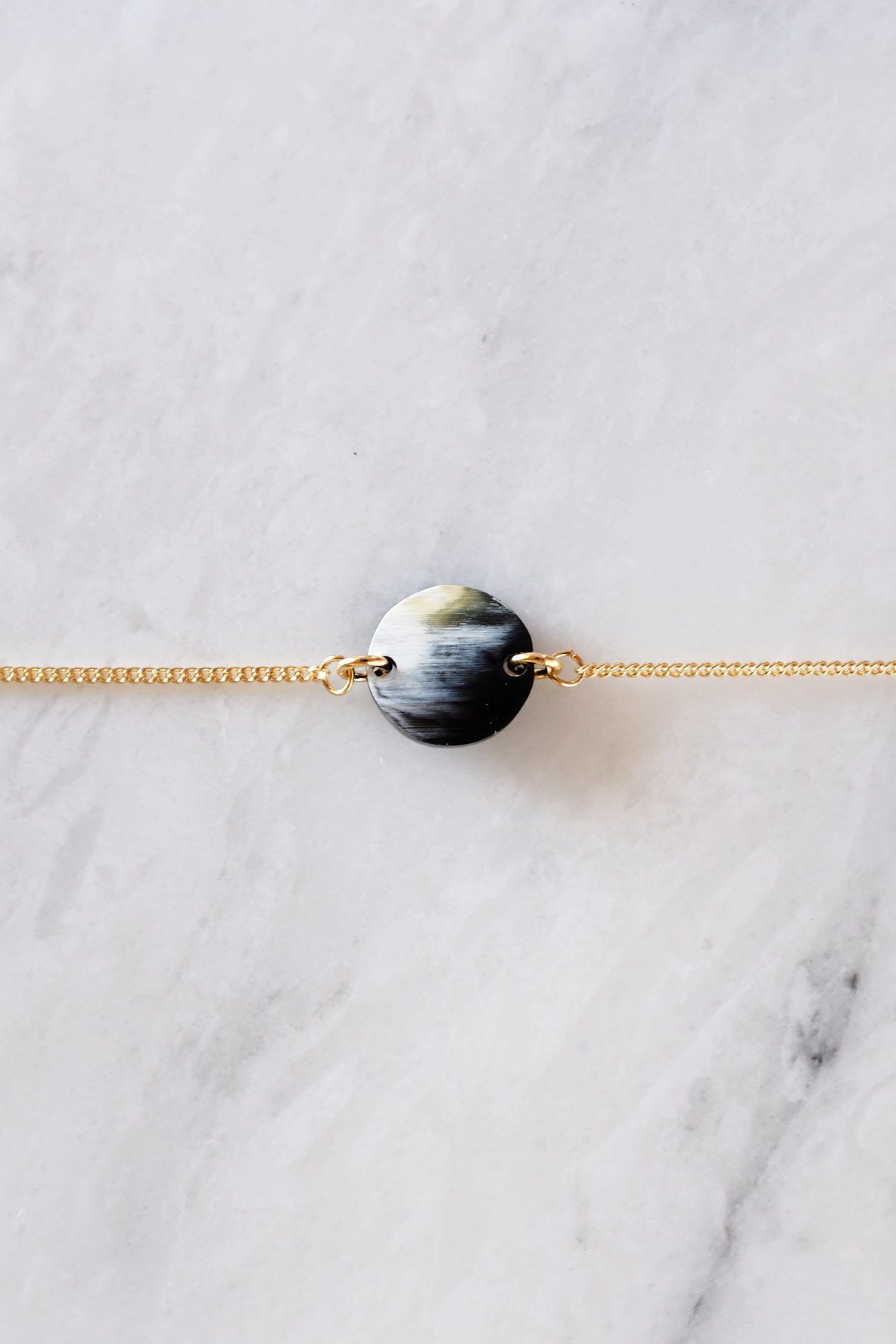 Tran Quoc Dainty Buffalo Horn Charm Bracelet on a marble surface with a gold curb chain.