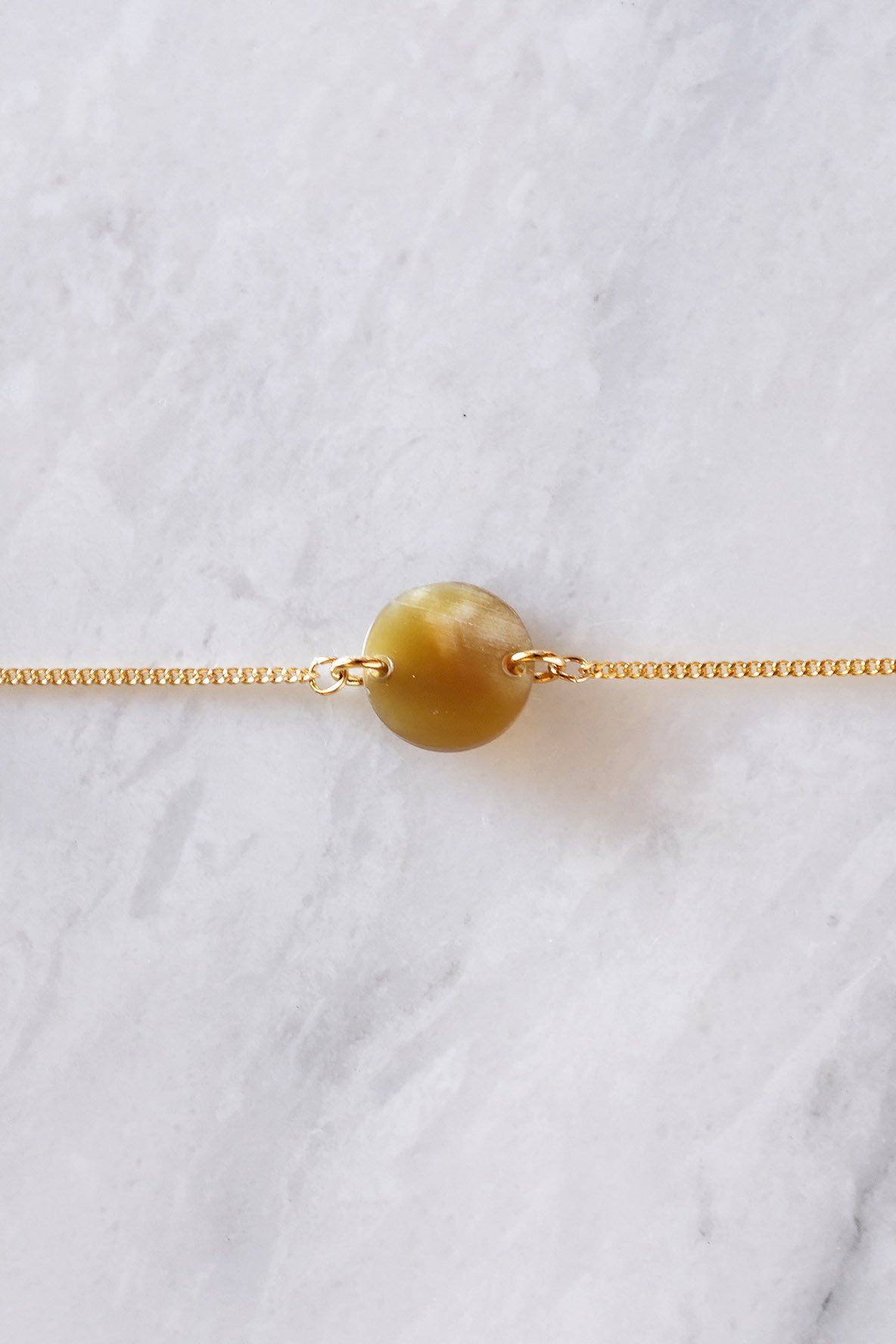 Tran Quoc Dainty Buffalo Horn Charm Bracelet with a circular horn charm on a dainty gold chain.