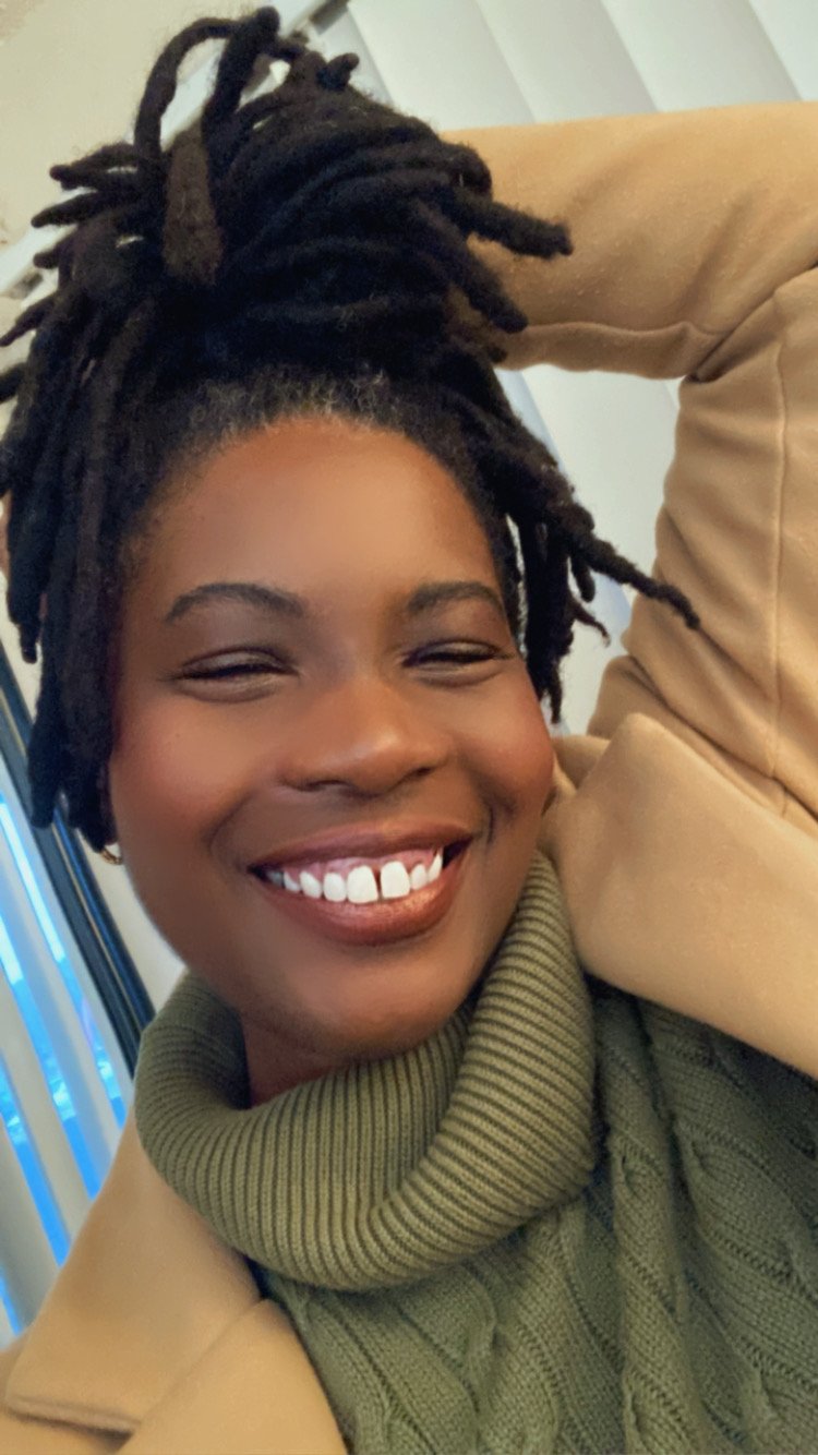 Smiling woman with dreadlocks wearing a green turtleneck sweater, showing joy and confidence.